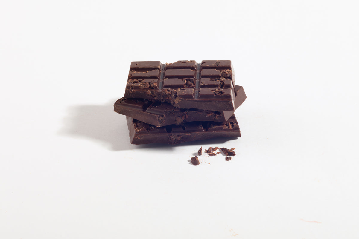 A stack of broken dark chocolate, cocoa nib chocolate bars with , photographed on a clean white background.