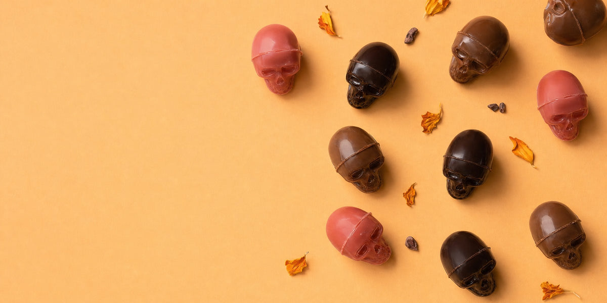 Hand-molded Halloween chocolate skulls in garnet, dark and milk chocolate on a pumpkin orange background